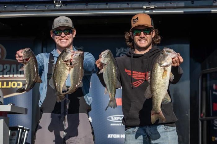 Two people hold a largemouth bass in each hand while posing for a photo.